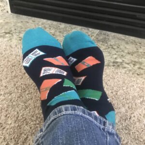 Cozy turquoise and navy socks on crossed feet with orange, green and turquoise books on them.